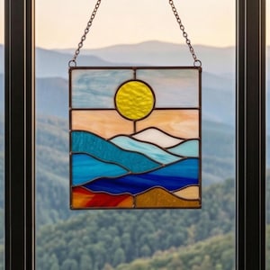 May include: Stained glass panel depicting a landscape with a yellow sun, blue water, and orange and tan land. The panel is rectangular with a chain for hanging. The design evokes a serene, natural scene.