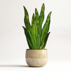 May include: A decorative, stained-glass plant in a beige ceramic pot. The plant features long, green leaves with dark outlines. The pot has a rounded shape and a textured surface, adding a touch of natural elegance to the design.