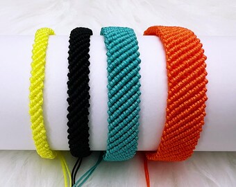Può includere: Quattro braccialetti dell'amicizia intrecciati in giallo, nero, turchese e arancione. I braccialetti sono realizzati con un motivo intrecciato e hanno una chiusura annodata.