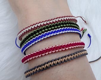 Può includere: Cinque braccialetti dell'amicizia colorati realizzati con corda intrecciata. I braccialetti sono in tonalità di rosso, rosa, verde, blu e marrone.
