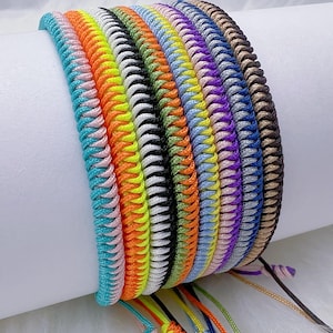 May include: A selection of braided bracelets in a range of colours. The bracelets feature shades of turquoise, pink, orange, yellow, white, black, light blue, purple, and brown. Each bracelet has adjustable cords with decorative knots.