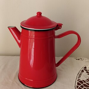 May include: A red enamel teapot with a white rim and a black handle. The teapot has a lid with a white rim and a black knob.