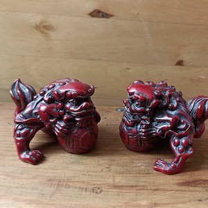 May include: Two red, intricately carved, mythical lion statues. The statues are in a crouching position with their heads turned towards each other.