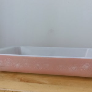 May include: A pink glass baking dish with a white floral design. The dish is made of Pyrex and is in good condition.