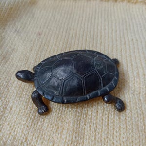 May include: A black turtle figurine with a detailed shell and legs. The turtle is made of metal and has a smooth, polished finish.
