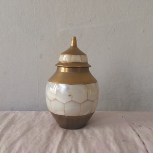 May include: A gold and white decorative jar with a lid. The jar is made of brass and has a mother-of-pearl inlay.