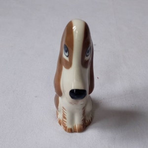May include: A ceramic figurine of a brown and white basset hound dog. The dog is sitting with its head tilted down and its eyes closed.