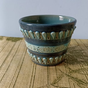 May include: A blue ceramic planter with a geometric design. The planter has a light blue glaze with a brown and white pattern.