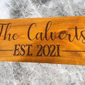 May include: A wooden sign with the text "The Calverts EST. 2021" in a brown font.