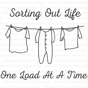 Op de afbeelding: Een zwart-witte lijntekening van kleding die aan een waslijn hangt. De kleding omvat een T-shirt, een romper en een shirt met lange mouwen. De tekst "Sorting Out Life One Load At A Time" staat boven de waslijn.