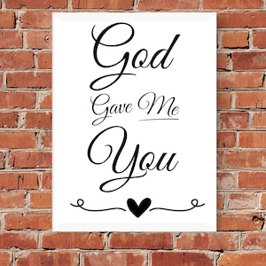 以下が含まれることがあります： 黒い文字で「God Gave Me You」と書かれた白い額装されたプリント。テキストの下に小さな黒いハートがあります。