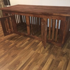 May include: A wooden dog crate with two doors and a top surface. The crate is made of dark brown wood and has a rustic look. The crate is sitting on a hardwood floor.