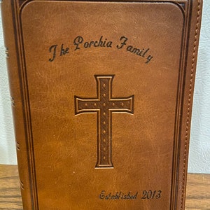 May include: A brown leather-bound journal with the inscription "The Porchia Family Established 2013" and a cross design embossed on the front cover.