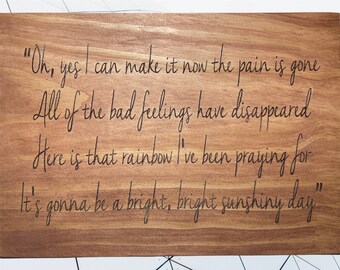 May include: A wooden cutting board with an engraved quote: "Oh, yes I can make it now the pain is gone All of the bad feelings have disappeared Here is that rainbow I've been praying for It's gonna be a bright, bright sunshiny day"