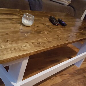 May include: A wooden coffee table with a dark brown stained top and white painted legs. The table has a simple, rustic design and is perfect for a living room or family room.