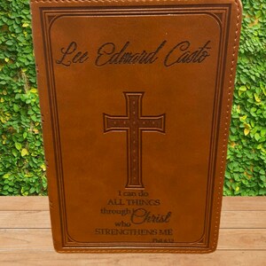May include: A brown leather-bound journal with a cross and the text "I can do ALL THINGS through Christ who STRENGTHENS ME Phil 4:33" engraved on the front. The name "Lee Edward Casto" is also engraved on the front.