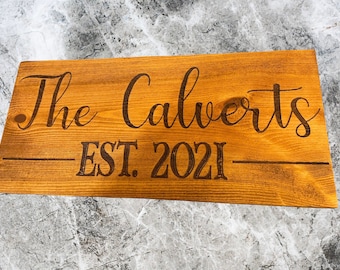 May include: A wooden sign with the text "The Calverts EST. 2021" in a brown font.