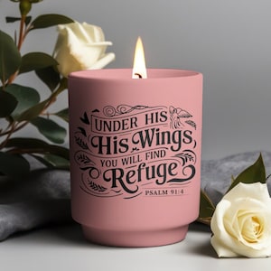 May include: A pink candle with a black inscription that reads "Under His Wings, You Will Find Refuge, Psalm 91:4".