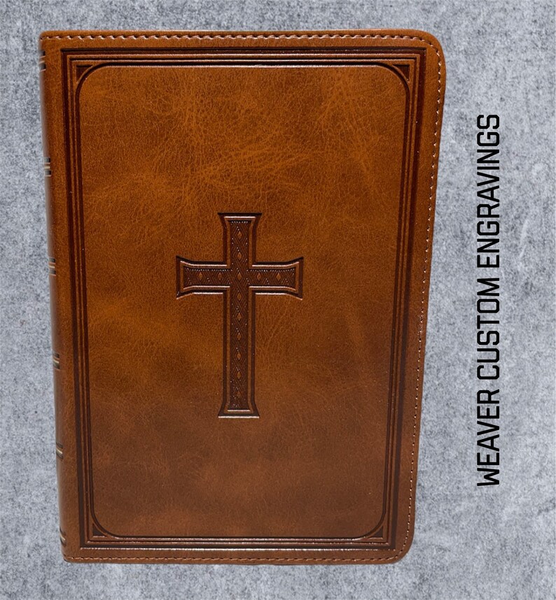 May include: A brown leather-bound journal with a cross embossed on the front cover. The journal has a gold-colored spine and is titled "WEAVER CUSTOM ENGRAVINGS".