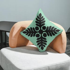 Op de afbeelding: Een mintgroen kussen met een zwart geometrisch ontwerp. Het kussen ligt op een lichtbruine en witte bank.