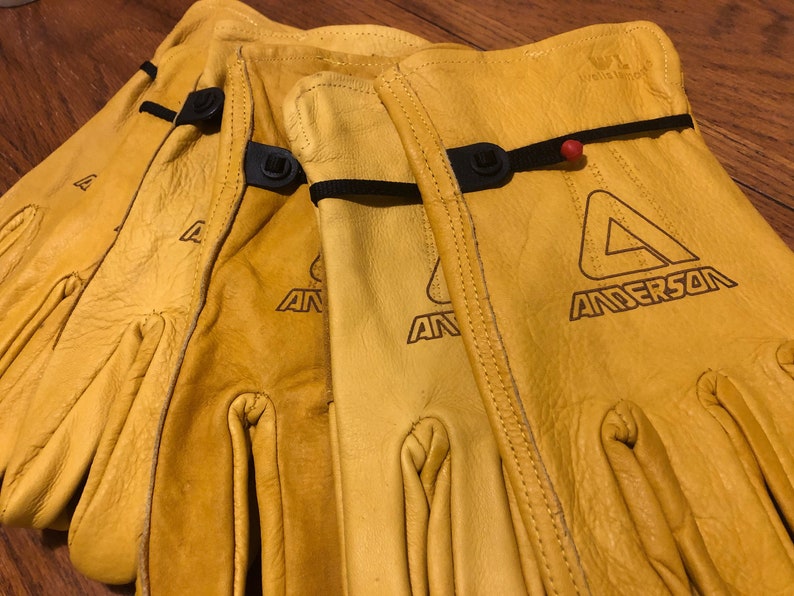 May include: Three pairs of yellow leather work gloves with black adjustable straps and the logo "Anderson" printed on the back of the gloves.