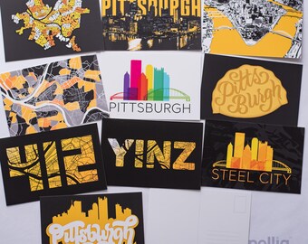Op de afbeelding: Een verzameling ansichtkaarten met Pittsburgh-thema. De ansichtkaarten tonen stadsgezichten, kaarten en tekst zoals "Pittsburgh", "Yinz" en "Steel City" in geel en wit tegen een zwarte achtergrond. Eén ansichtkaart is blanco.