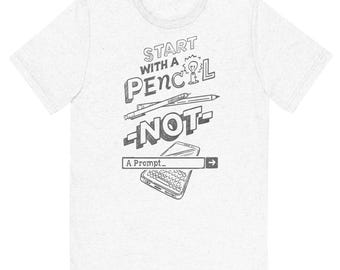 May include: A light grey heathered t-shirt featuring a dark grey graphic print. The design includes the text "START WITH A PENCIL NOT A PROMPT" alongside illustrations of a pencil, a lightbulb, and a smartphone with a keyboard and cursor.