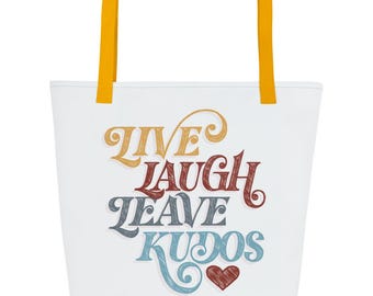 May include: A white tote bag with mustard yellow handles featuring the text LIVE LAUGH LEAVE KUDOS in a multi-coloured, stylised font with a small red heart icon at the bottom. The lettering uses a cross-hatched texture in gold, red, and blue.