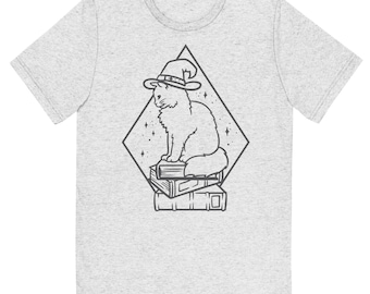 May include: A light heather grey short-sleeve t-shirt featuring a black line art graphic of a fluffy cat wearing a pointed witch hat, sitting atop a stack of two books, all enclosed within a diamond-shaped frame with small star accents.