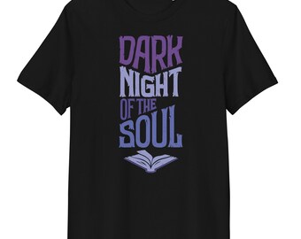 May include: A black short-sleeved t-shirt featuring a graphic print in purple and light blue. The text reads DARK NIGHT OF THE SOUL in a stylised font, positioned above an illustration of an open book. The design is centred on the chest.
