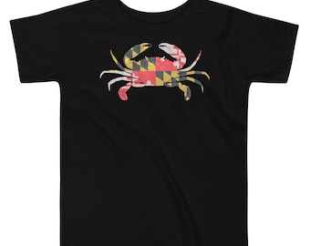 May include: A black short-sleeved t-shirt featuring a graphic of a crab centred on the chest. The crab is filled with the red, white, black, and yellow geometric pattern of the Maryland state flag, including its distinct cross and heraldic designs.
