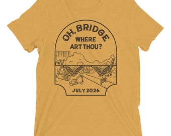 May include: A mustard yellow short-sleeved t-shirt featuring a black line art graphic of a bridge construction site. The text reads OH, BRIDGE WHERE ART THOU? and JULY 2026. The illustration includes cranes, a shipping container, and road barriers.