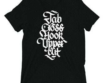 May include: A black short-sleeved t-shirt featuring white distressed-style lettering centred on the chest. The text reads "Jab Cross Hook Upper Cut" in a stylised gothic font, arranged vertically in a stacked, decorative block format.