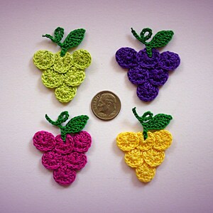 May include: Four crocheted grape clusters in different colors: green, purple, pink, and yellow. Each cluster has a green stem and leaves.