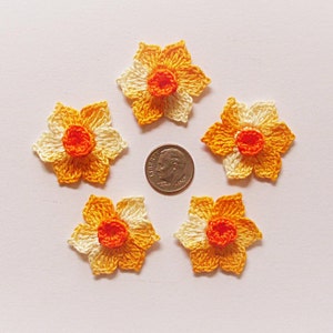 May include: Five crocheted daffodil flowers in shades of yellow, orange, and white. The flowers are approximately the size of a US dime.