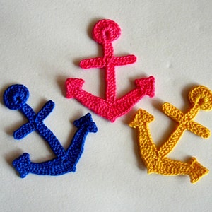 Puede incluir: Tres anclas de ganchillo en diferentes colores: azul, rosa y amarillo. Las anclas son todas del mismo tamaño y forma.