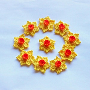 Könnte beinhalten: Ein Kreis aus zehn gehäkelten Narzissen in Gelb und Orange. Die Narzissen sind in einem Kreis angeordnet, wobei die orangenen Zentren nach außen zeigen.