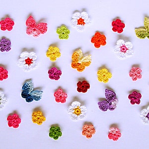 Könnte beinhalten: Eine Sammlung gehäkelter Blumen und Schmetterlinge in verschiedenen Farben, darunter Weiß, Rosa, Rot, Orange, Gelb, Grün, Blau und Lila. Die Blumen und Schmetterlinge sind alle klein und zart und in einem zufälligen Muster auf einem weißen Hintergrund angeordnet.