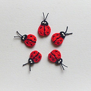 Könnte beinhalten: Fünf rote gehäkelte Marienkäfer mit schwarzen Punkten und weißen Augen. Die Marienkäfer sind sternförmig auf einem weißen Hintergrund angeordnet.