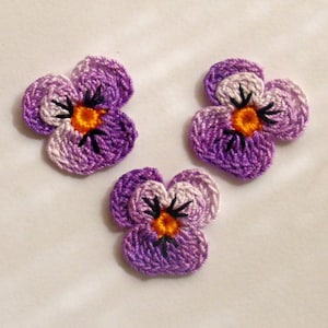 May include: Three crocheted purple and white pansies with orange centres. The pansies are handmade and have a delicate, vintage look.