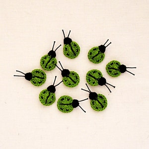 Może przedstawiać: Dziewięć zielonych biedronek wykonanych na szydełku z czarnymi główkami i nóżkami. Biedronki są ułożone w kółko na białym tle.