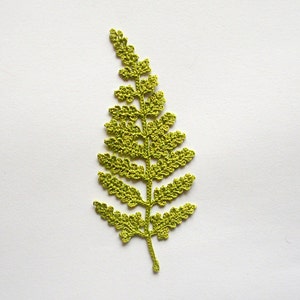 May include: A green crocheted fern leaf with a delicate, intricate design.