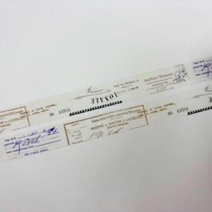 May include: Decorative washi tape with a vintage aesthetic. The tape features a repeating pattern of old documents, signatures, and stamps in shades of beige, black, and blue. The tape is partially rolled, revealing the design.