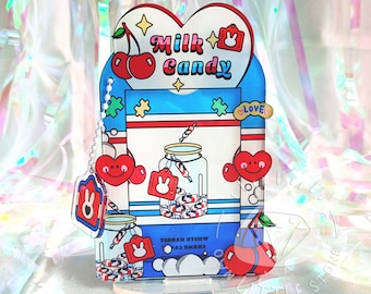 May include: A heart-shaped acrylic stand with a blue, red, and white design. The stand features a cartoon illustration of a jar filled with candy, a cherry, and the text "Milk Candy".