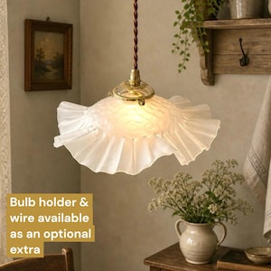 May include: A pendant light featuring a frosted, ruffled glass shade with a textured surface. The shade is attached to a brass-coloured metal fixture and hangs from a twisted brown cord. The light emits a warm glow from within the glass.