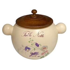 May include: Cream ceramic container with a wooden lid and side handles. The container is decorated with floral illustrations in purple, pink, and white, and the words "Table Nette" are written in script.