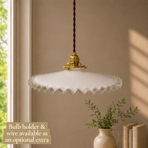 May include: A pendant light featuring a wide, white, ruffled-edge glass shade with a clear, scalloped trim. The shade is suspended by a dark brown twisted fabric cord and connected to a polished brass fixture. Text reads: Bulb holder & wire available as an optional extra.
