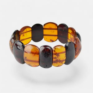 Peut inclure: Un bracelet composé de perles d'ambre dans des tons de brun, orange et noir. Les perles sont de forme ovale et ont une finition polie.