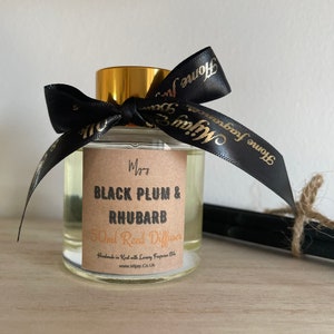 May include: A 50 ml reed diffuser bottle with a black ribbon and gold lid. The label reads "Myjay Black Plum & Rhubarb 50ml Reed Diffuser Handmade in Kent with Luxury Fragrance Oils www.Mijay.Co.Uk"