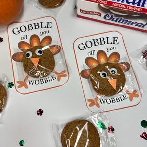 Pode incluir: Guloseimas de biscoitos com tema de Ação de Graças. Cada biscoito é embalado em uma embalagem transparente e decorado com um rosto de peru e as palavras "Gobble till you Wobble". Uma caixa de biscoitos Little Debbie Oatmeal também é visível.